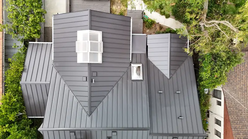 Dark standing seam metal roof with skylights and several gables, seen from above