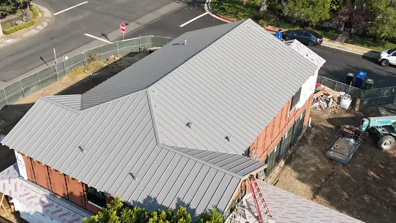 Gray standing seam metal roof being completed on a house under renovation