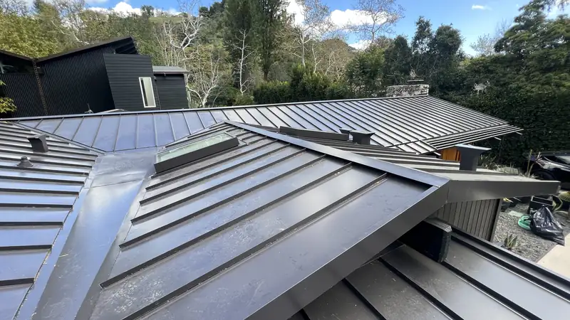 Standing seam metal roof panels meeting at a hip beside a skylight